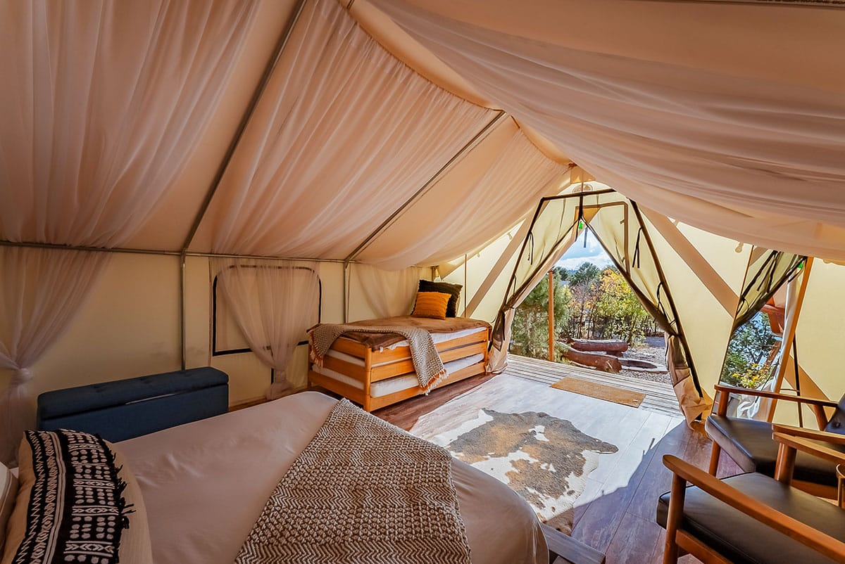 Interior of a spacious glamping tent with two beds and a view of nature.